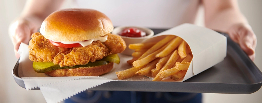 A person holding a tray with a crispy chicken sandwich and fries on it