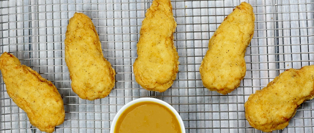 Prebreaded chicken tenders cooling on a grate
