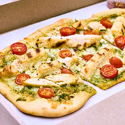 A flatbread pizza topped with sliced chicken, pesto, and tomatoes