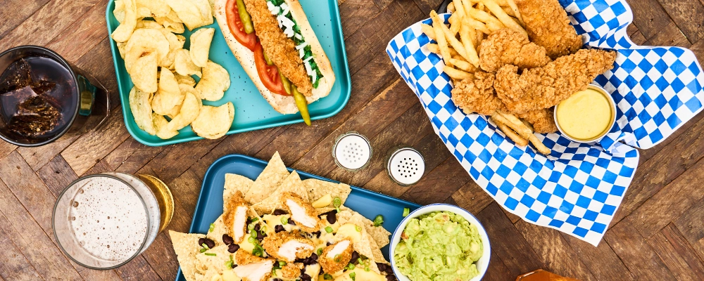 A top down view of nachos, a chicken tender basket, and a chicken Chicago dog