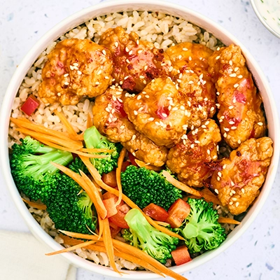 A bowl filled with rice, chicken, broccoli, carrots, tomato, and sauce