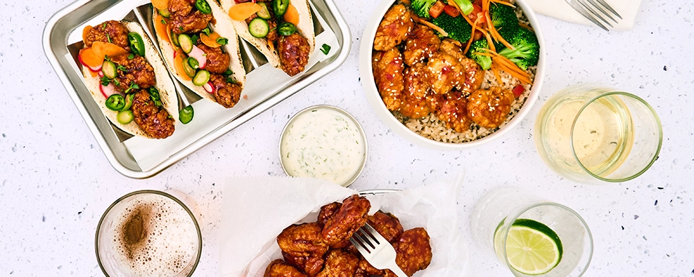 A top down view of a boneless wings basket, tacos, and a grain bowl