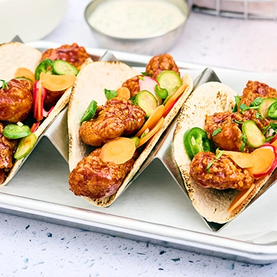 Tacos filled with boneless wings, jalapeno, cucumber, carrot, and radish