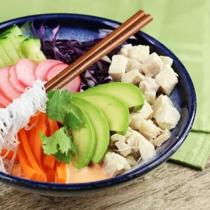 A bowl with diced chicken, avocado, carrots, rice noodles, radish, cucumber, cabbage, and sauce
