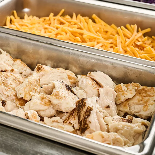 A closeup of a salad bar with pulled chicken and shredded cheese