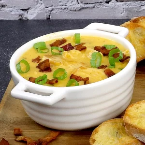 A cup of beer cheese soup, topped with bacon and green onion