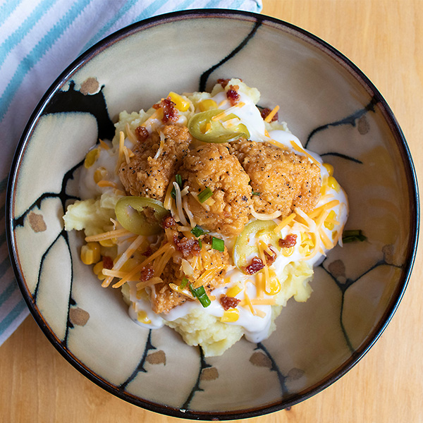 Mashed potatoes, `boneless chicken wings, cheese, and toppings on a bowl