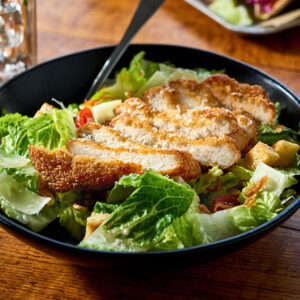 Bowl of caesar salad topped with a sliced, breaded chicken filet