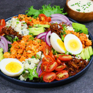 Cobb salad on a plate with Buffalo-Style diced chicken, eggs, tomato, bleu cheese, avocado, and lettuce.