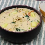 A bowl of soup with gnocchi, chicken, spinach, carrots, and tomatoes.