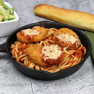 Chicken nuggets over spaghetti in a small cast iron pan