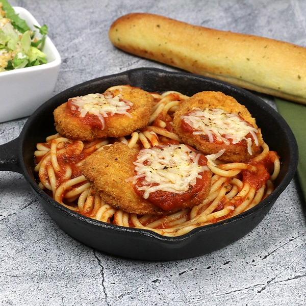 Chicken nuggets over spaghetti in a small cast iron pan
