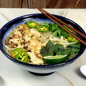 A bowl of chicken pho with noodles, pulled chicken, basil, jalapenos, and broth