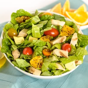 A bowl of salad with lettuce, grilled chicken, cherry tomatoes, and citrus dressing