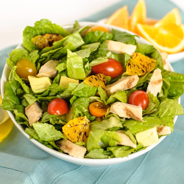 A bowl of salad with lettuce, grilled chicken, cherry tomatoes, and citrus dressing