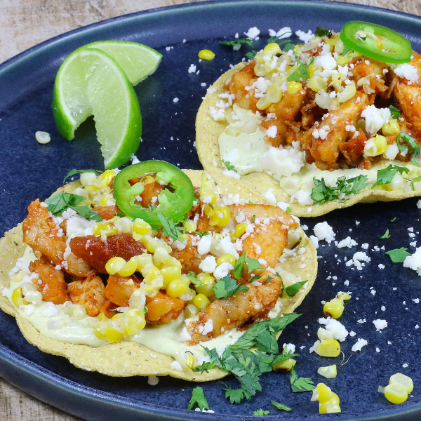 Two tostadas on a plate, covered in sliced chicken and elote