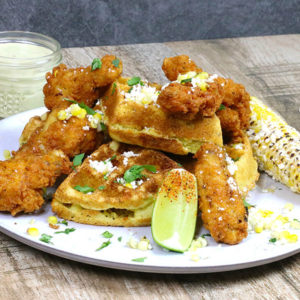 Waffle covered in elote toppings and chicken wings on a plate