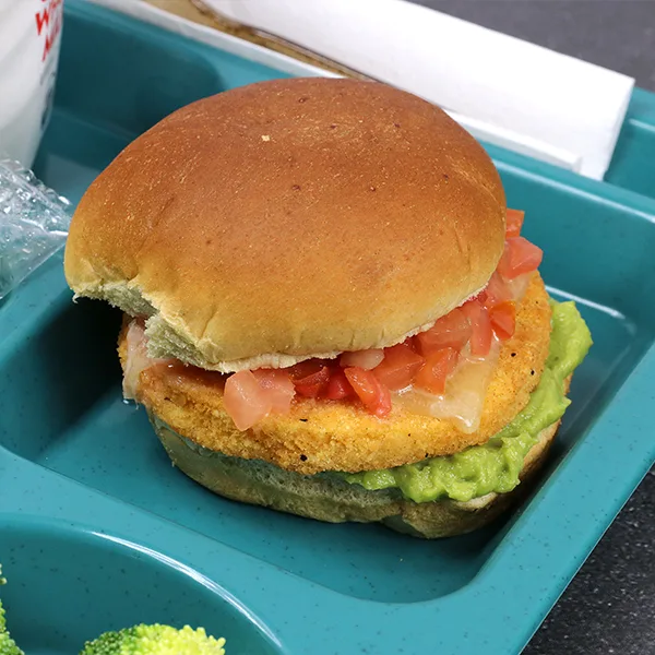 A chicken pattie with guacamole, cheese, and pico de gallo on a school tray