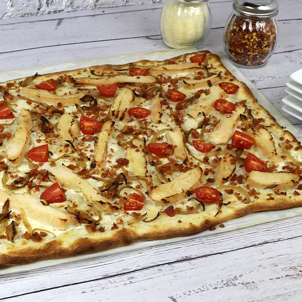 A full Flammkuchen pizza with chicken, onions, and grape tomatoes on a table