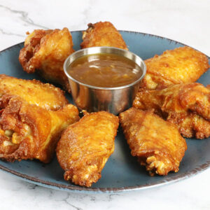 Unbreaded wings on a plate surrounding a dish of hot honey orange ginger sauce