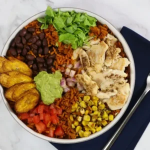 A burrito bowl filled with rice, corn, chicken, lettuce, plantain, guacamole, and more
