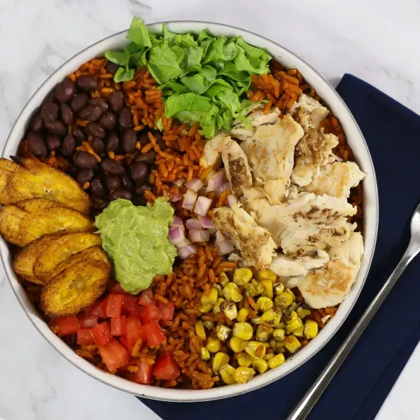 A burrito bowl filled with rice, corn, chicken, lettuce, plantain, guacamole, and more