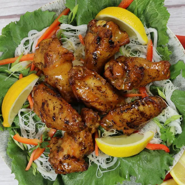 Chicken wings on a bed of rice noodles, lettuce leaves, and lemon slices