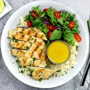 A bowl with rice, salad greens, a sliced chicken filet, and lemongrass vinaigrette