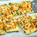 A pan of breadsticks, topped with Buffalo-style diced chicken, pickled veggies, and cheese