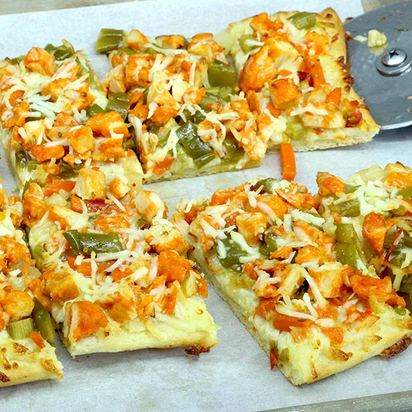 A pan of breadsticks, topped with Buffalo-style diced chicken, pickled veggies, and cheese