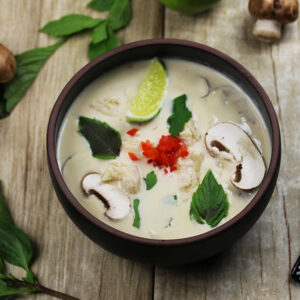 A bowl of chicken coconut soup with mushrooms, lime, and cilantro